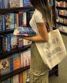 a woman carrying a book in front of a bookshelf filled with lots of books