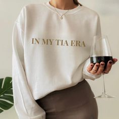 a woman holding a glass of wine wearing a sweatshirt with the words in my tiaera printed on it