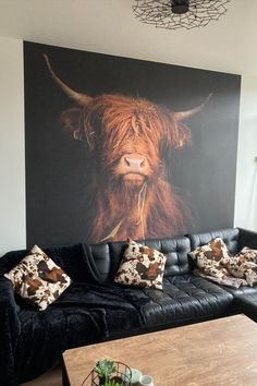 a living room with black leather couches and a cow painting on the wall