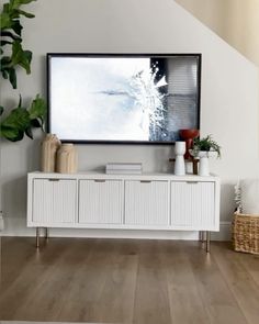 a tv mounted on the wall above a white cabinet in a room with wooden floors