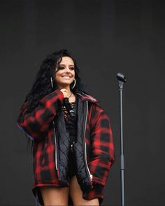 a woman standing in front of a microphone and wearing a red plaid jacket with her hands on her hips