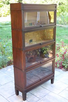 an old wooden cabinet with glass doors on the top and bottom shelf is sitting in front of a grassy area