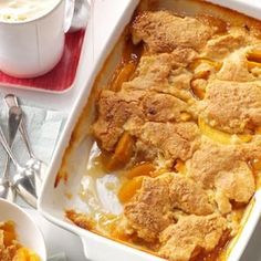 a casserole dish filled with peach cobbler next to a cup of coffee