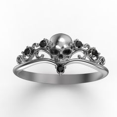 a silver ring with a skull and black stones on the front, sitting on a white surface