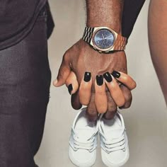 two people holding hands with black and white manies on their fingers, one wearing a watch