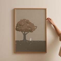 a woman holding up a painting with a tree on it