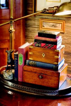 a stack of books sitting on top of a wooden table next to a lamp and framed pictures