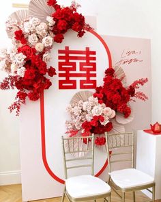 two white chairs sitting next to each other in front of a wall decorated with red and white flowers