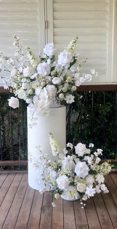 a white vase filled with flowers sitting on top of a wooden floor next to a fence