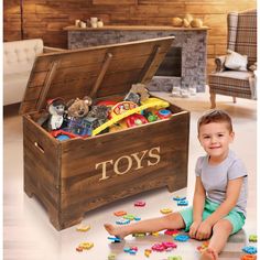 a little boy sitting on the floor next to a toy chest with toys in it