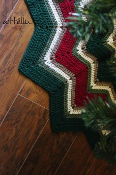 a crocheted christmas tree skirt is on the floor next to a fir tree