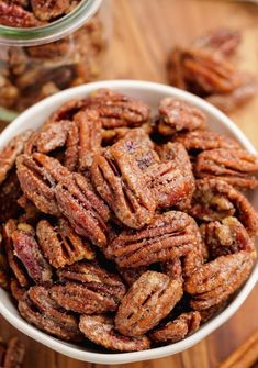 a white bowl filled with pecans sitting on top of a wooden table next to cinnamon sticks