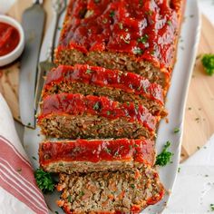 sliced meatloaf with marinara sauce on a white platter next to a fork