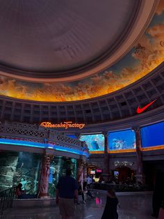 people are walking around in the lobby of a building with many large screens on the ceiling