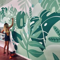 a woman standing next to a wall covered in green leaves and plants on it's side