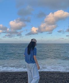 a woman standing on top of a beach next to the ocean under a cloudy blue sky