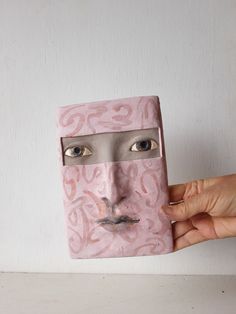 a person holding up a pink mask with eyes