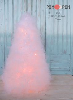 a white christmas tree with pink lights in front of a blue door and wooden floor