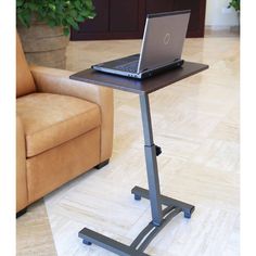 a laptop computer sitting on top of a metal stand in front of a brown couch