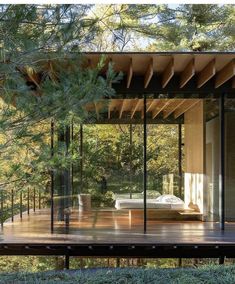 a house in the woods with glass walls and wood flooring, surrounded by trees