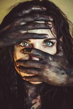 a woman covered in mud covering her face and hands with both hands over her eyes