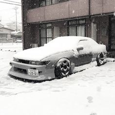 a car covered in snow parked on the side of a street next to a building