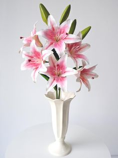 a white vase filled with pink flowers on top of a table