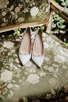 a pair of white shoes sitting on top of a green floral covered chair next to a plant