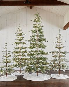 three small evergreen trees in white pots on a wooden table with snow covered ground and wood beams