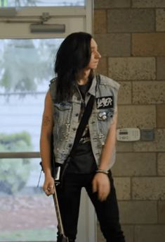 a person with a guitar standing in front of a brick wall and window holding a skateboard