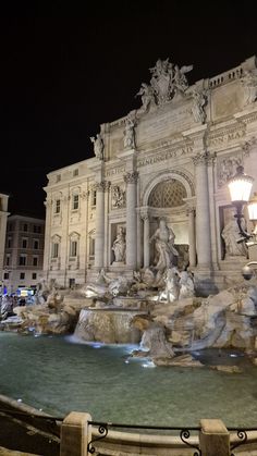 a fountain in front of a building with statues and lights on it's sides