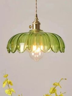 a green glass light hanging from a ceiling fixture with yellow flowers in the foreground