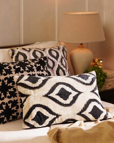 a bed with black and white pillows on top of it next to a night stand