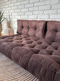 a brown couch sitting on top of a rug next to a white brick wall and potted plant