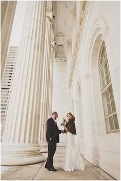 a bride and groom standing in front of an old building holding hands with each other