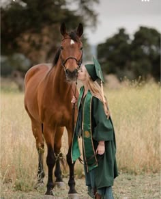 a woman in a green gown standing next to a brown horse and kissing her face