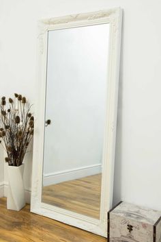 a mirror sitting on top of a wooden floor next to a vase filled with flowers