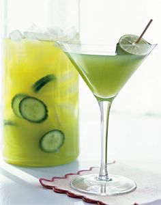 two glasses filled with cucumber and limeade on a white tablecloth next to each other