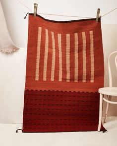 a red and white rug hanging on a clothes line with a chair in the background