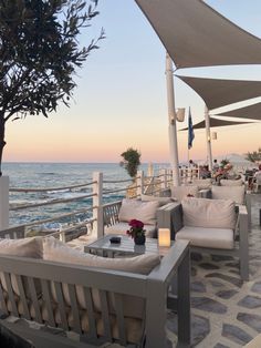 an outdoor seating area next to the ocean at sunset with umbrellas and tables on it