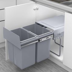 two trash cans in the corner of a kitchen with white cabinets and gray counter tops