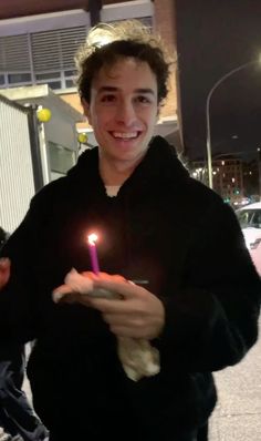 a young man holding a lit candle in his right hand and smiling at the camera