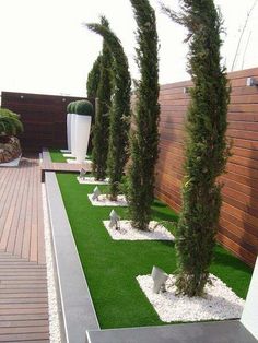 a row of trees in front of a wooden wall and artificial grass on the ground