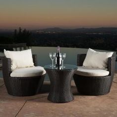 two wicker chairs and a table with wine glasses on it in front of a pool