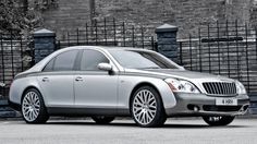 a silver car parked in front of a brick wall and gated area with black iron railings