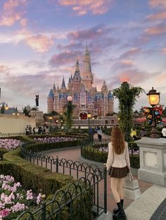 a woman is standing in front of a castle with flowers on the ground and bushes around her