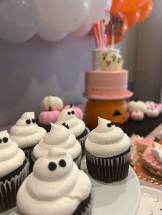 cupcakes with white frosting and black eyes are on a plate in front of balloons