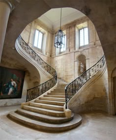 an ornate staircase in the middle of a building with two large windows and a painting on the wall