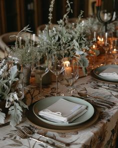 the table is set with place settings and silverware, candles, and greenery