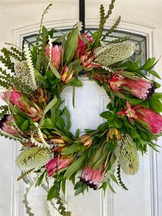 a wreath with pink flowers and green leaves hanging on a white door frame, decorated with greenery